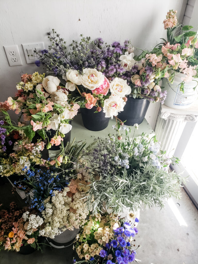 Buckets of DIY flowers picked from a local flower farm in a pastel color palette including fluffy peonies .