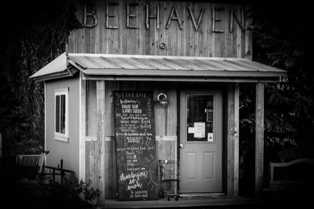 A black and white photo of a saloon type building that is a farm stand that sells DIY flowers.